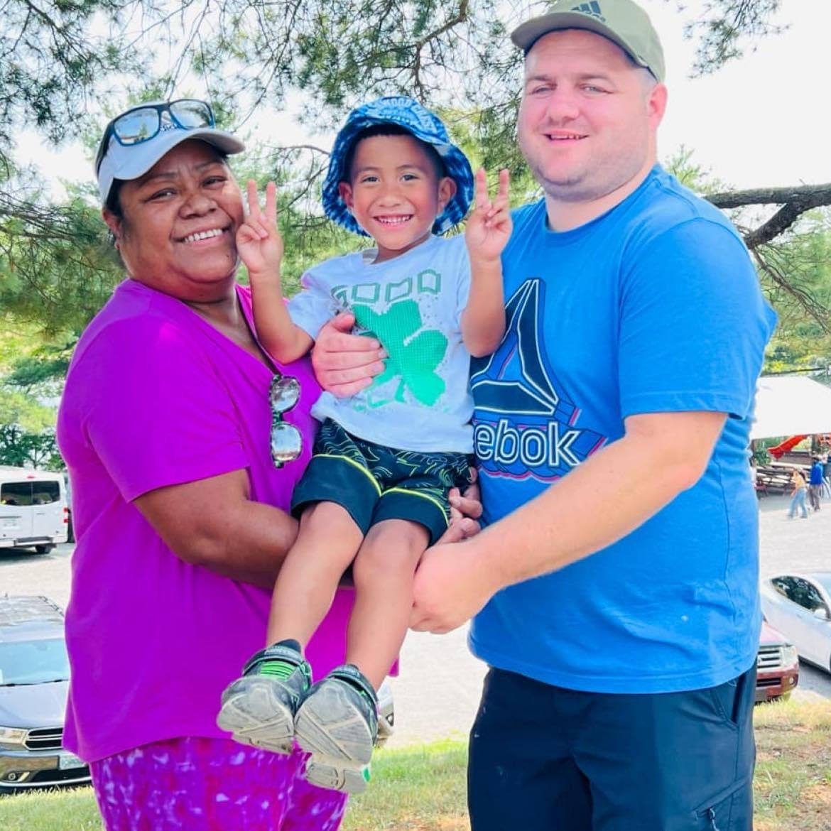 A family of three, including a smiling child, posing for a photo in a park.